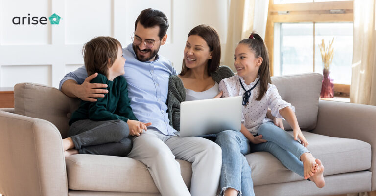 Family of four (mom, dad, two daughters) sitting on a couch, smiling.